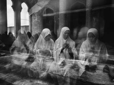 Double exposure black and white street photography of barefoot pilgrims praying in a mosque